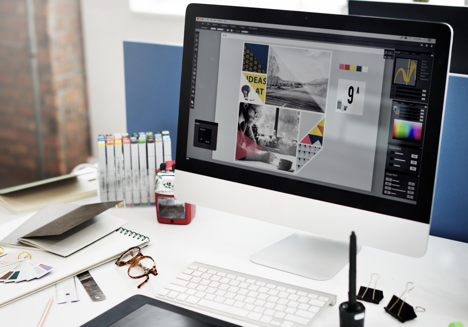 Designer's desk with a computer showing a brand moodboard, colour swatches, and design tools