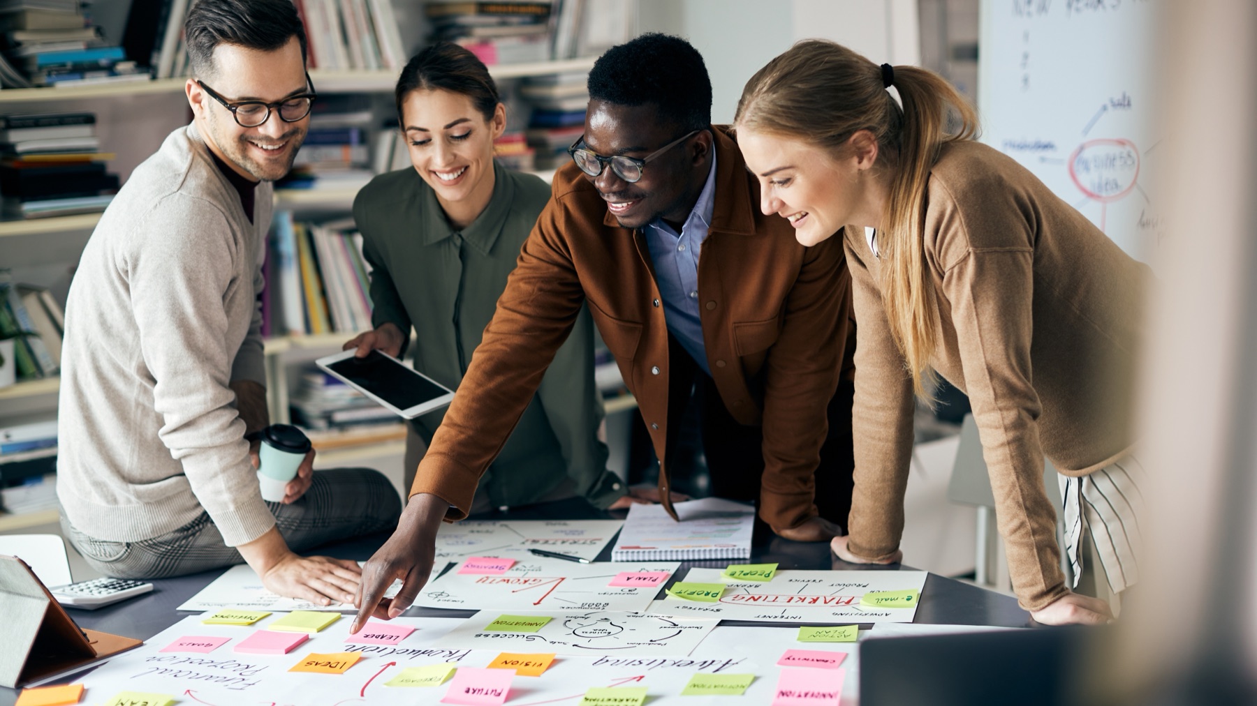 Four colleagues leaning over a table covered in sticky notes and hand-drawn strategy diagrams during a planning session