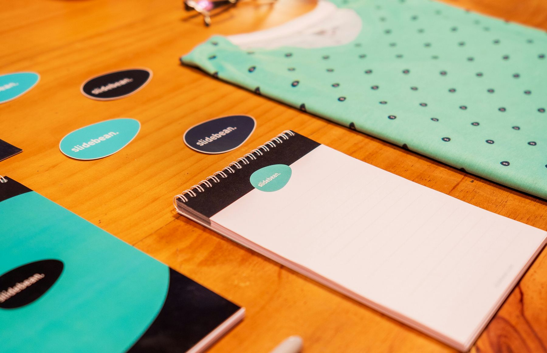 Branded stickers, a notebook, and a folded patterned t-shirt laid out on a wooden desk