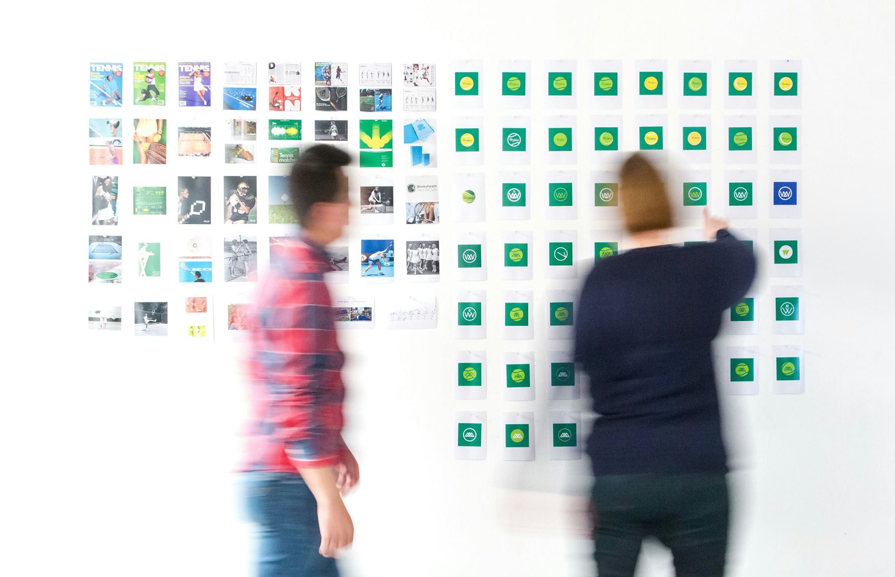 Two people reviewing pinned-up logo concepts and brand moodboards on a studio wall