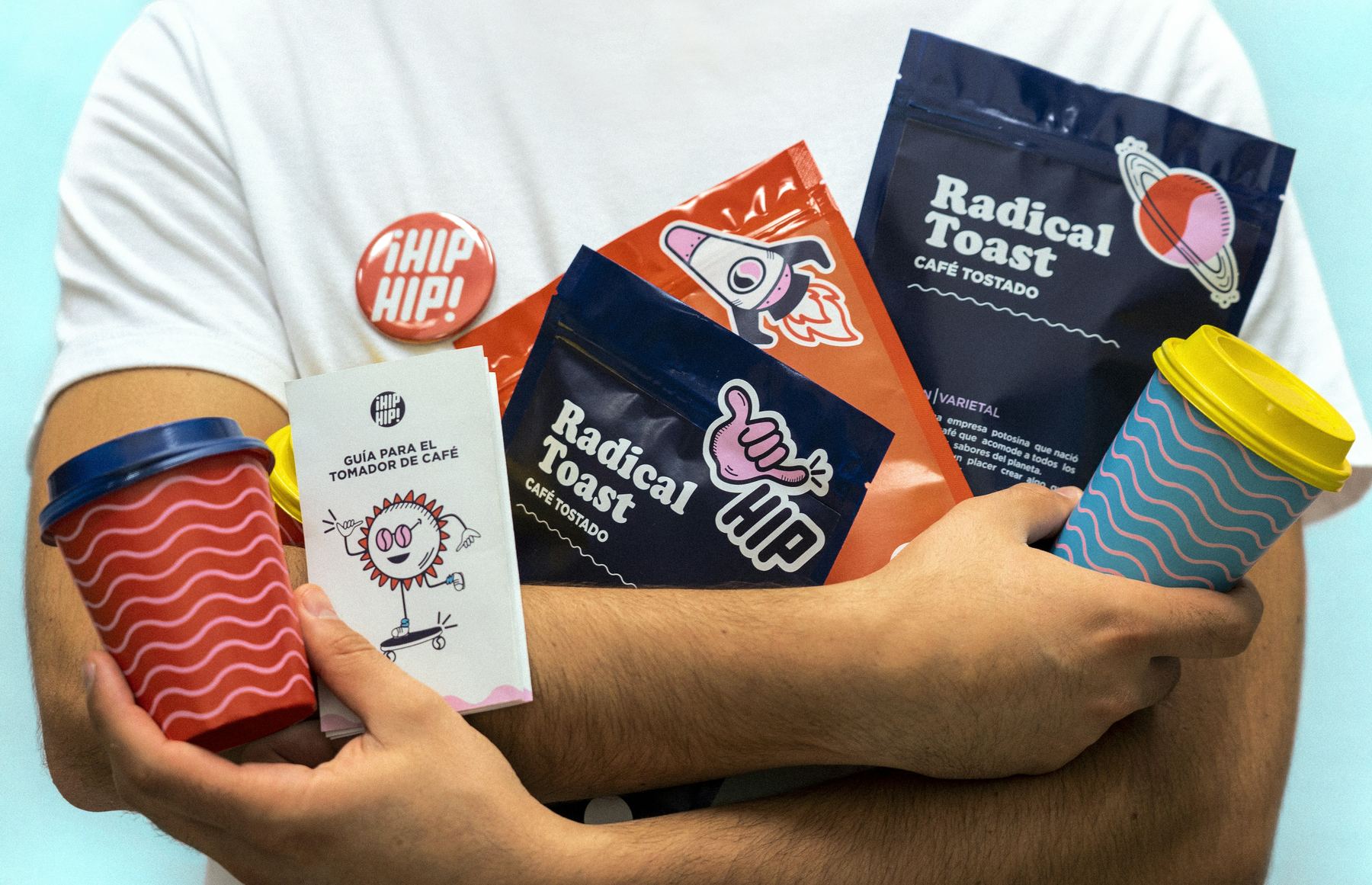 A bundle of launch materials, including packaging, a branded cup, and a printed guide, held in someone's arms